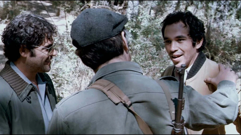 Che Part 2 (Guerrilla) (2008) movie still: medium — Three men stand together in a dense outdoor area with natural vegetation background. A man in a…
