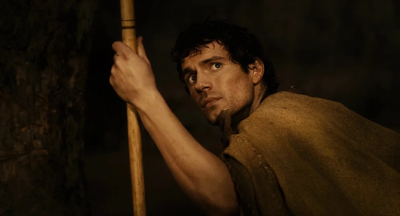The Immortals (2011) movie still: medium — Dark environment with a single tree trunk visible in the left foreground. A man leans against the tree…