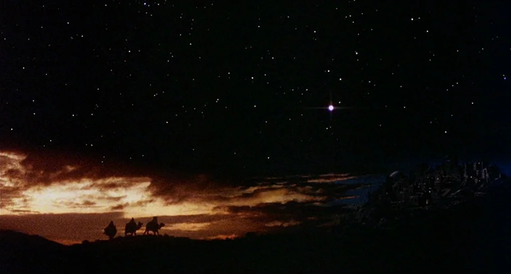 Life of Brian (1979) movie still: establishing — A vast, dark desert landscape stretches under a star-filled night sky at twilight. Three camels…
