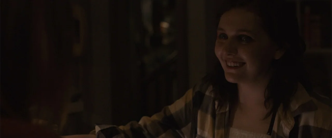 Maggie (2015) movie still: medium — A dimly lit indoor space with low-key lighting and obscured architectural details. A woman in a plaid shirt…