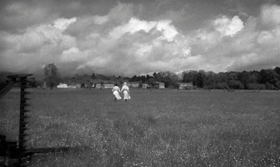 Thérèse Desqueyroux (1962) movie still: wide — A wide expanse of open grassy land under a sky filled with large clouds. Two figures in light-colored…