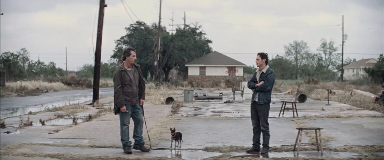 Killing Them Softly (2012) movie still: fullbody — An abandoned suburban concrete lot with utility poles and sparse dry grass. Two men stand apart…