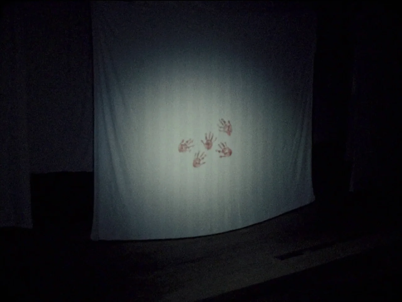 The Devil’s Doorway (2018) movie still: wide — A white fabric sheet hangs in a pitch-black, cavernous interior space. Five distinct reddish…