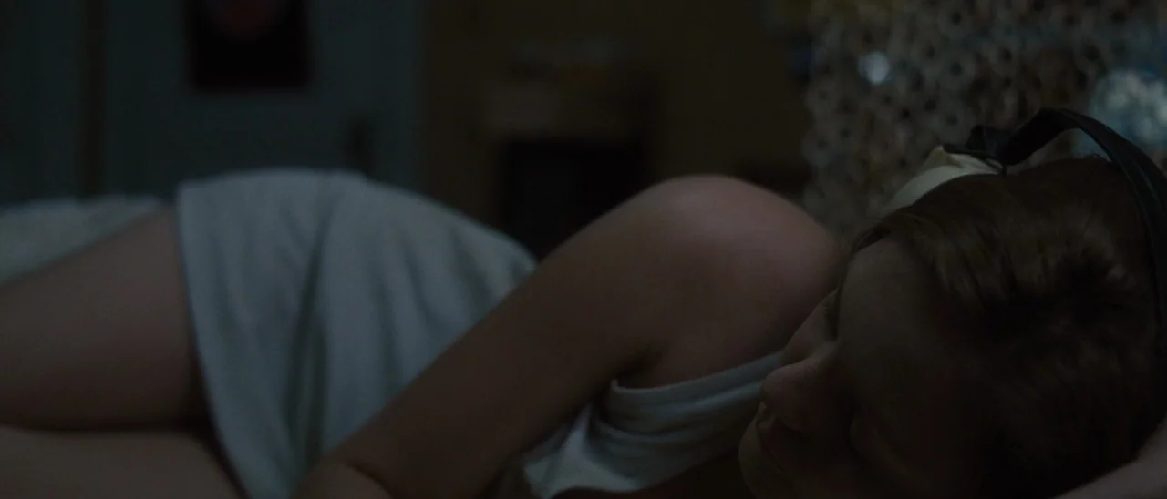 Halloween (2007) movie still: closeup — A dark bedroom interior at night features a person resting under low light. A woman sleeps on her side…