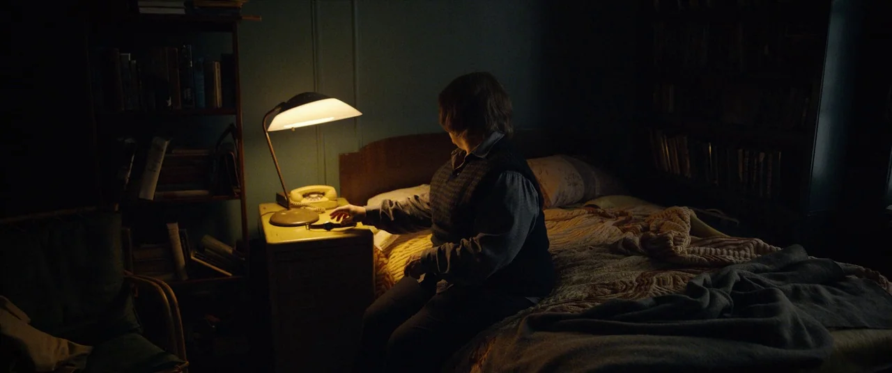 Can You Ever Forgive Me? (2018) movie still: medium — A dark, cluttered room with bookshelves filled with books on either side of a bed. A person…