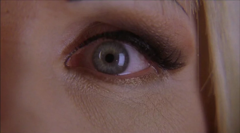 Hedwig and the Angry Inch (2001) movie still: closeup — A close-up shot focuses on a human eye with distinct green-gray irises. Thick dark eyeliner…