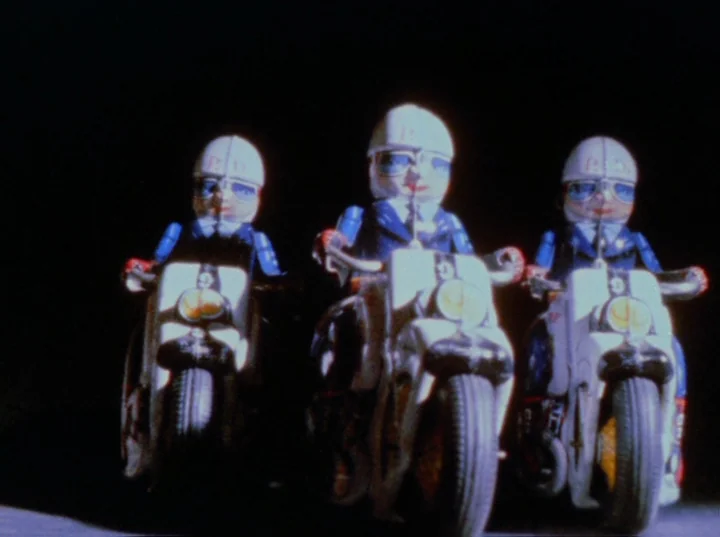 Scorpio Rising (1963) movie still: medium — Three vintage tin toy police officers ride motorcycles in a row against black space. The small toys are…