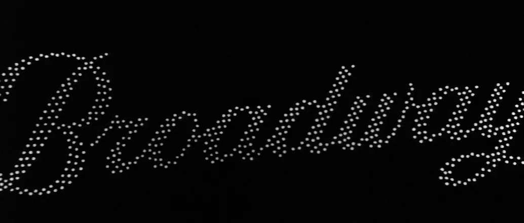 Manhattan (1979) movie still: closeup — The word Broadway is spelled out in bright, individual white light bulbs. The sign is set against a solid,…
