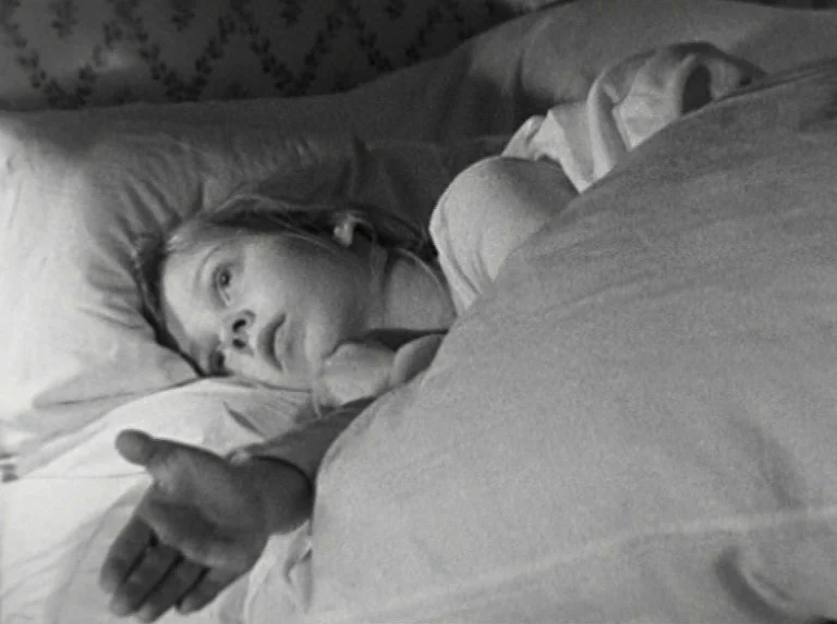 Alice in the Cities (1974) movie still: closeup — A dark bedroom with patterned wallpaper is visible in the upper corner. A young girl lies under a…