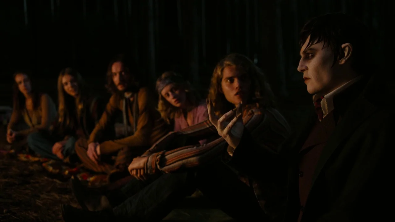 Dark Shadows (2012) movie still: medium — A group of young adults sits on the ground in a dark forest at night. A pale, dark-haired man in Victorian…