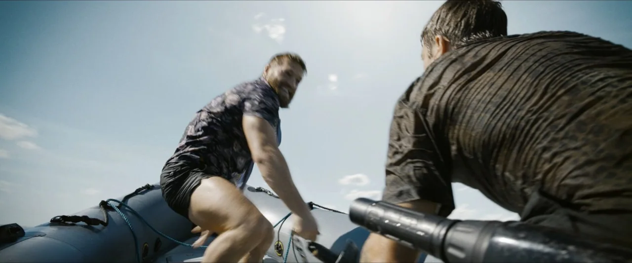 Road House (2024) movie still: medium — Two men in an inflatable boat navigate open water under a bright clear sky. The man in the foreground…