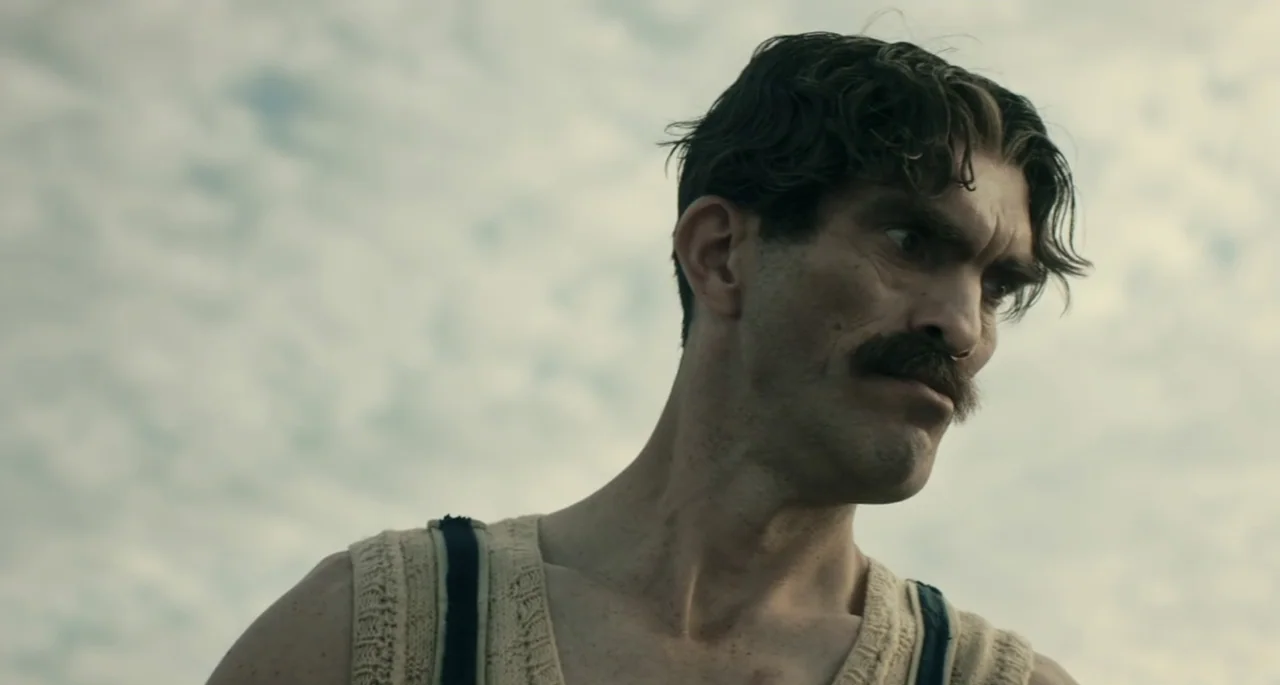 Pinocchio (2022) movie still: closeup — An open sky with light clouds serves as the background for a man outdoors. A man with a dark moustache and…
