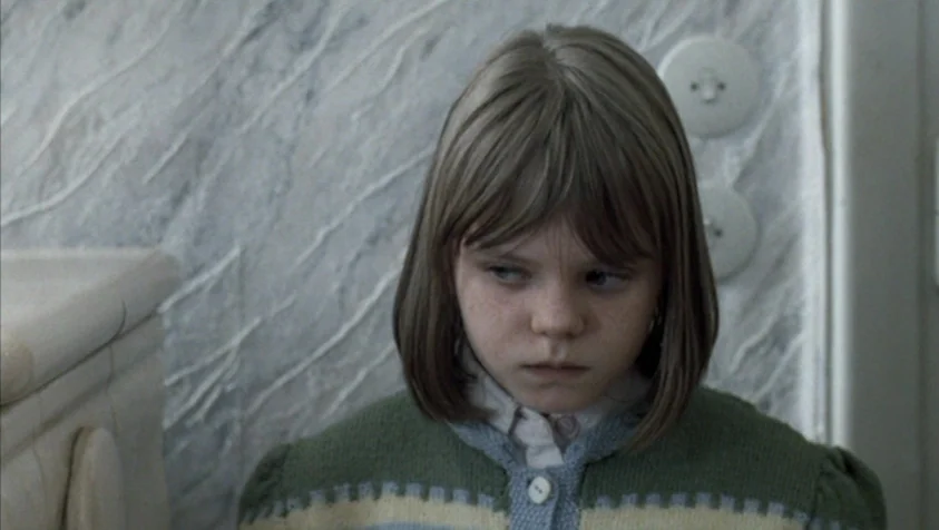 71 Fragments of a Chronology of Chance (1994) movie still: closeup — A child stands before a wall with light-colored textured wallpaper and circular…
