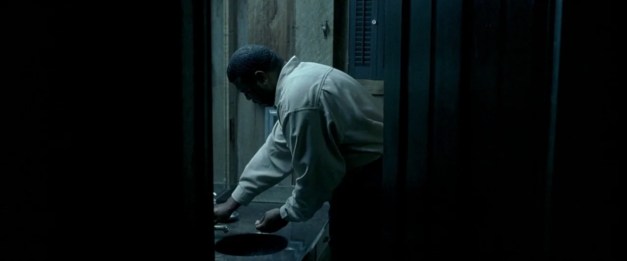 Ballast (2008) movie still: medium — A dark bathroom features simple walls and a modest sink setup. A man washes his hands while facing away from…