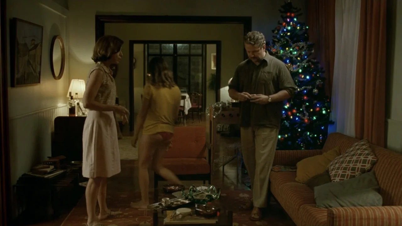 I'm Still Here (2024) movie still: fullbody — A 1970s style living room features a decorated Christmas tree in the corner. Three people stand in the…
