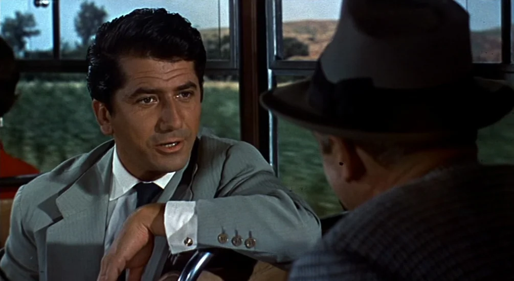 The Man Who Knew Too Much (1956) movie still: medium — The interior of a moving train car shows windows with blurred landscape in the back. A man in…