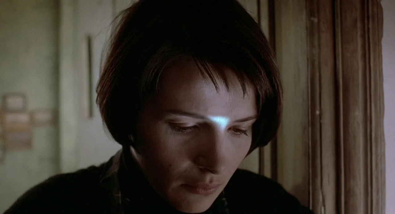 Three Colours: Blue (1993) movie still: closeup — A dimly lit interior space with a paneled wooden door frame in the background. A woman with short…