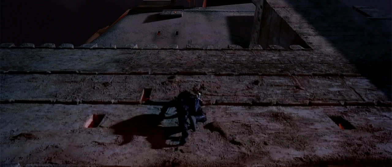 The Scorpion King (2002) movie still: wide — A dark stone castle wall rises against a night sky with small glowing apertures. A lone armored figure…