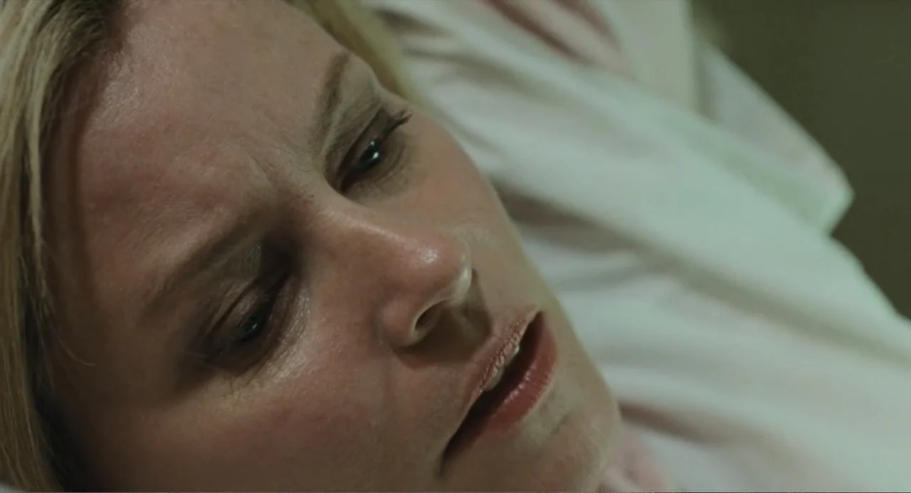 Call Jane (2022) movie still: closeup — A hospital setting with a blurred, pale, out-of-focus background. A woman in a white garment rests with her…