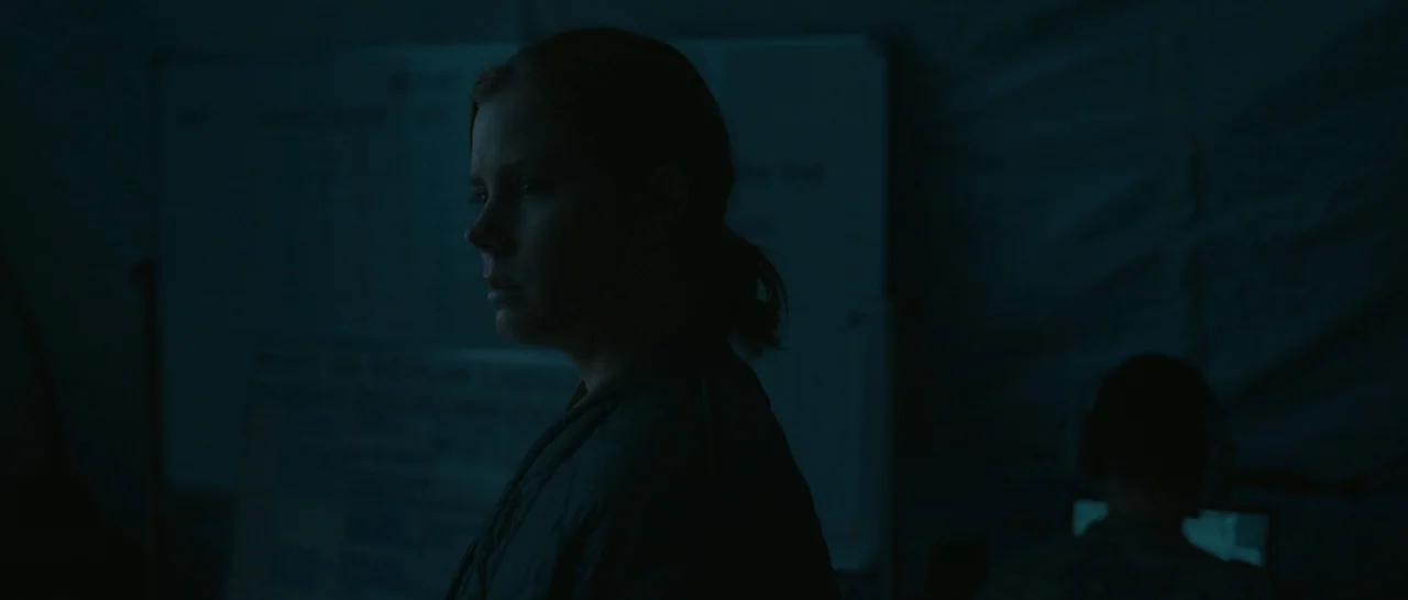 Arrival (2016) movie still: medium — A dimly lit, tented interior features textured fabric walls and a whiteboard in back. A woman stands in profile…