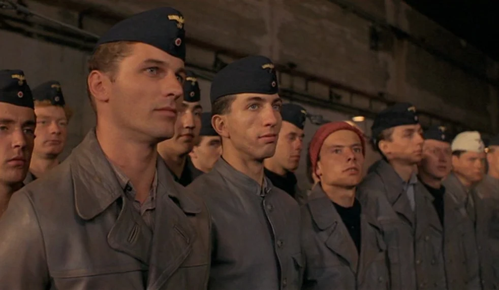 Das Boot (1981) movie still: medium — A group of men stand in formation inside a dimly lit concrete structure. The men wear matching grey uniforms…