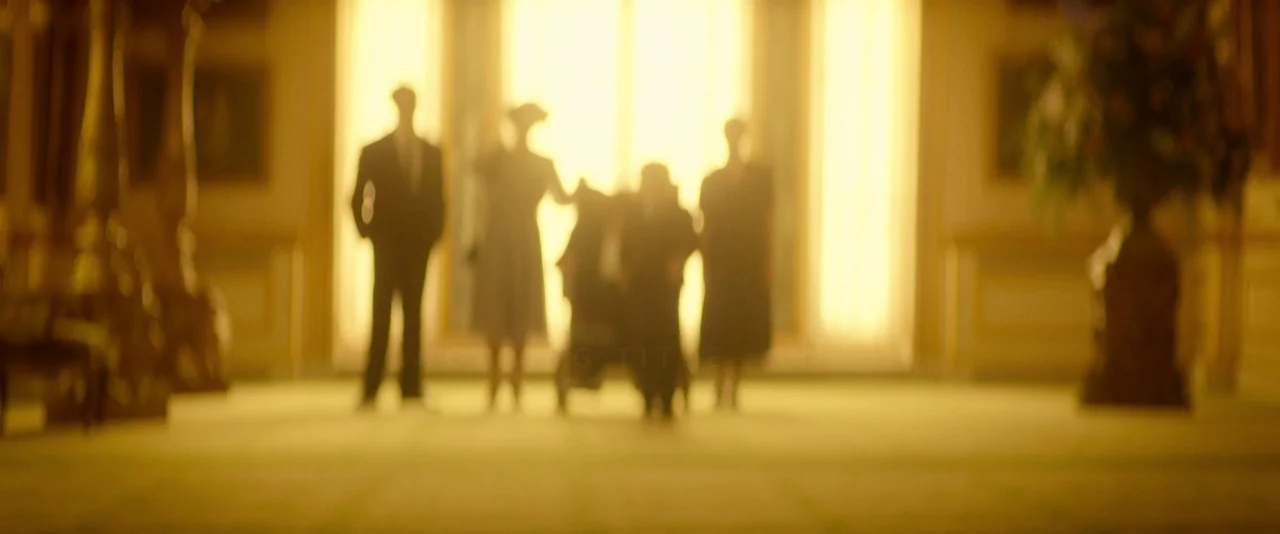 The Theory of Everything (2014) movie still: wide — A grand hallway with high windows and a bright, glowing golden light source. Four figures stand…