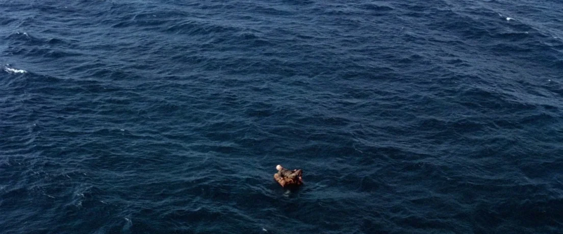 Papillon (1973) movie still: establishing — A vast expanse of deep blue ocean waves stretches across the entire frame. A single small brown life…