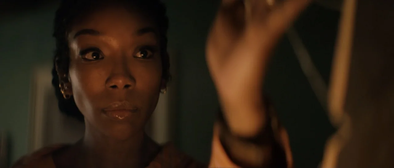 The Front Room (2024) movie still: closeup — A dark bedroom interior with a woman partially visible in the frame. The woman reaches her hand toward…