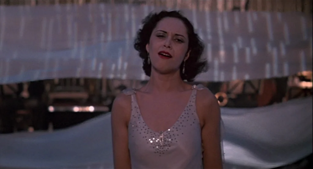 The Cotton Club (1984) movie still: medium — A theatrical setting features flowing fabric drapes backgrounded by a dark, cluttered stage area. A…