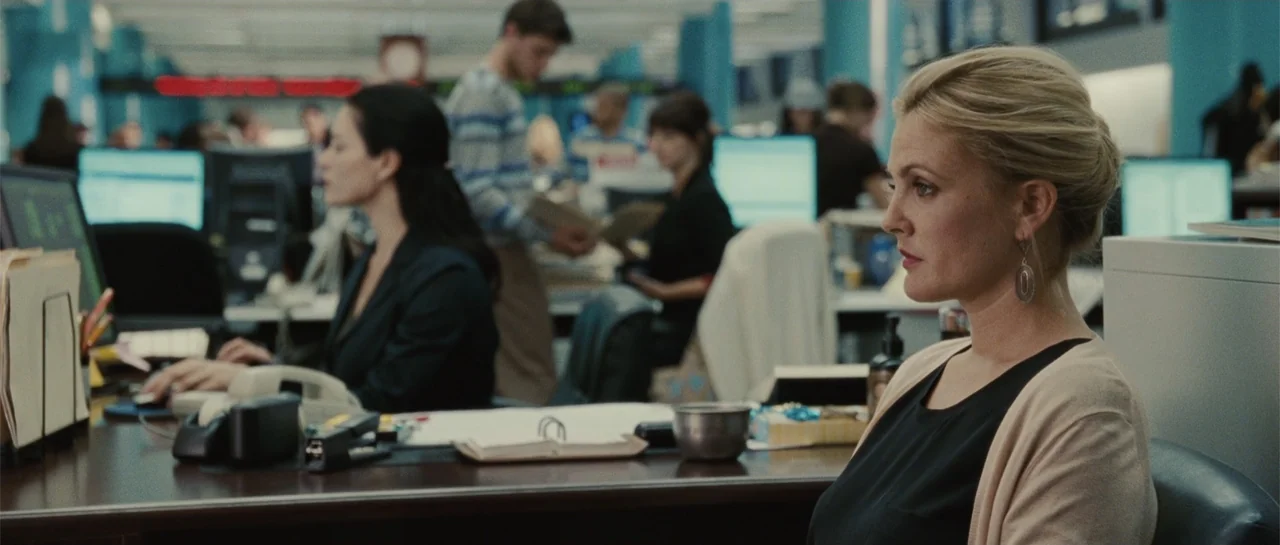 Going the Distance (2010) movie still: medium — A busy open plan workspace features rows of desks with computer monitors and papers. A blonde woman…