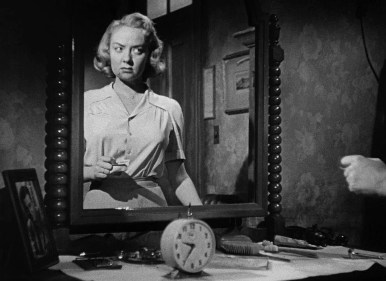The Set-Up (1949) movie still: medium — A dimly lit room containing a wooden vanity table with a large framed mirror. A woman stares intently at her…