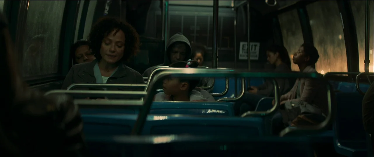 Birth/Rebirth (2023) movie still: medium — A dimly lit passenger cabin of a city bus with rows of blue plastic seats. Several passengers sit…