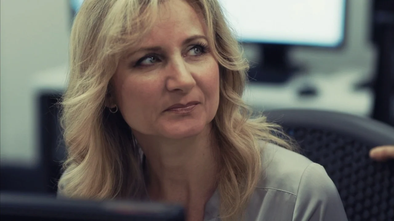 You Might Get Lost (2021) movie still: closeup — A modern office environment with blurred computer monitors visible in the background. A woman with…