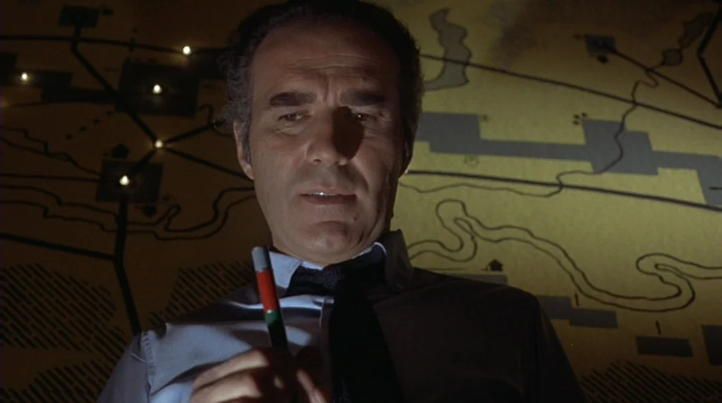 Danger Diabolik (1968) movie still: medium — A dark military operations center features a large illuminated map mounted on a wall. A man stands in…