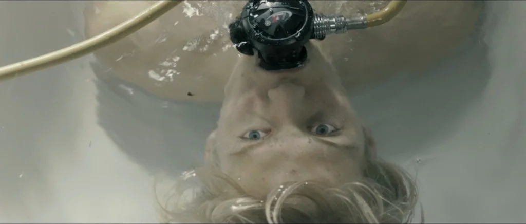 Lasting (Nieulotne) (2013) movie still: closeup — A white ceramic container filled with water reflects ambient overhead light. A young man lies…