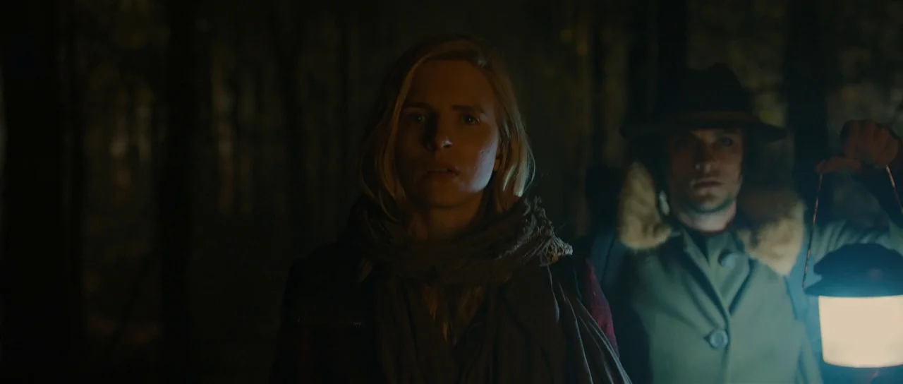 The East (2013) movie still: medium — A dark, wooded environment surrounds a man and woman at night. The pair stands close together while the man…