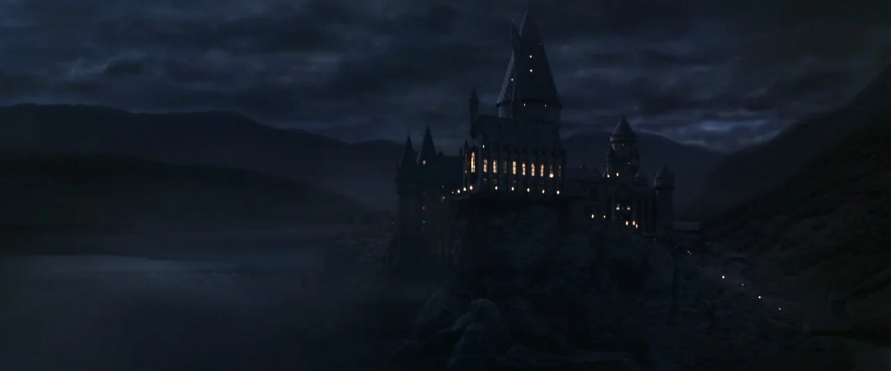 Harry Potter and the Chamber of Secrets (2002) movie still: establishing — A stone castle with multiple towers sits atop a rugged cliff edge at…