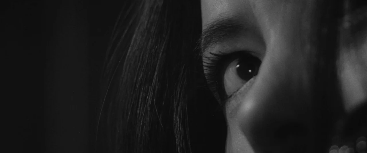 Carmen From Kawachi (1966) movie still: closeup — A close-up frame shows a portion of a human face in deep shadow. A single eye looks into the frame…
