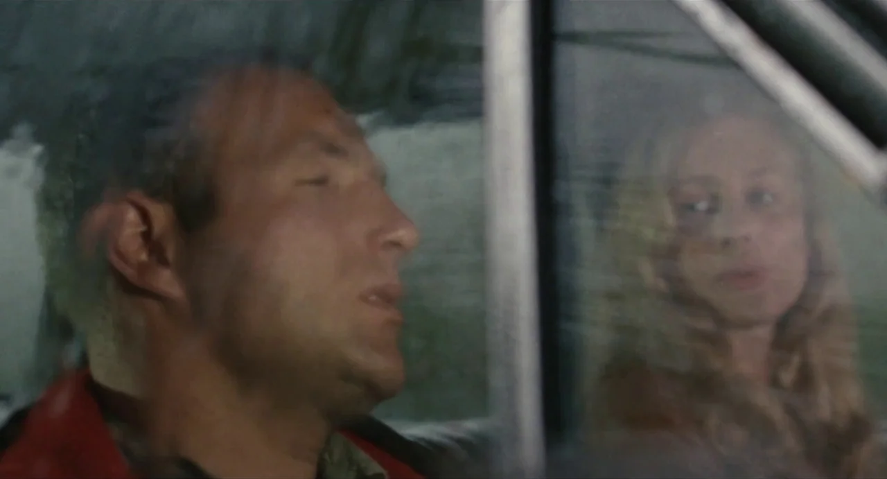 The Rain People (1969) movie still: medium — A man and a woman sit inside a car on a rainy day. Reflections appear on the car window glass obscuring…