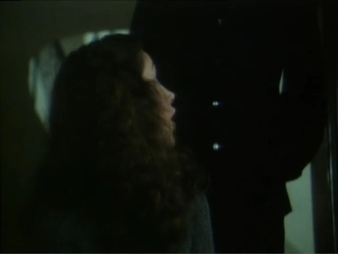 Curtains (1995) movie still: medium — A dark interior hallway with minimal light sources casting deep shadows across the walls. A woman looks upward…
