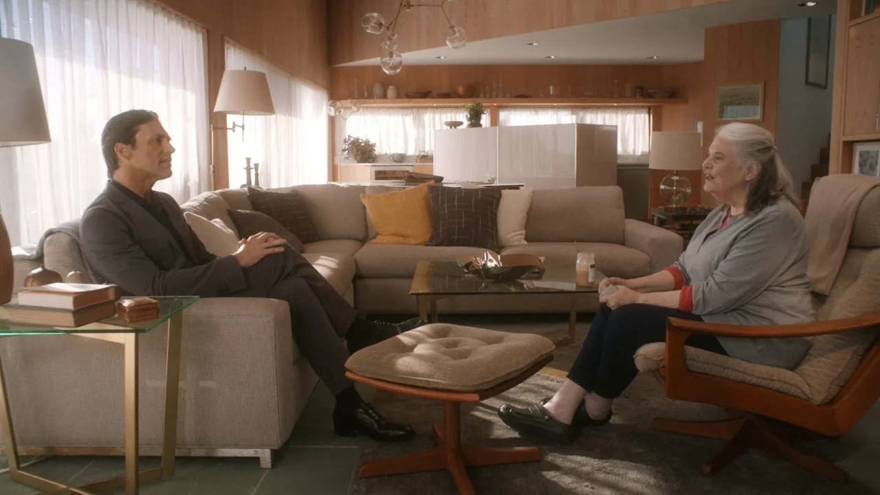 Marjorie Prime (2017) movie still: wide — A mid-century modern living room features wood-paneled walls and a large, comfortable beige sofa. A man…