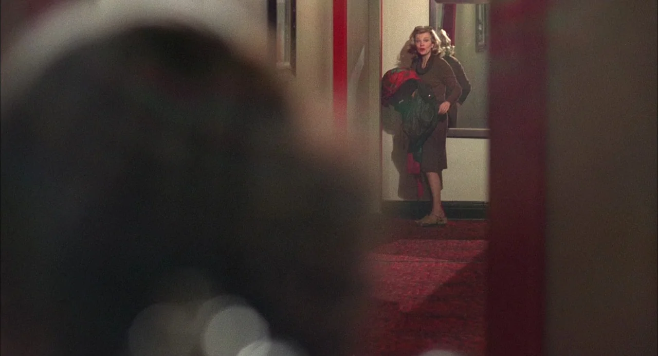 Opening Night (1977) movie still: medium — A hotel corridor features red patterned carpeting and plain off-white walls. A woman stands in the frame…
