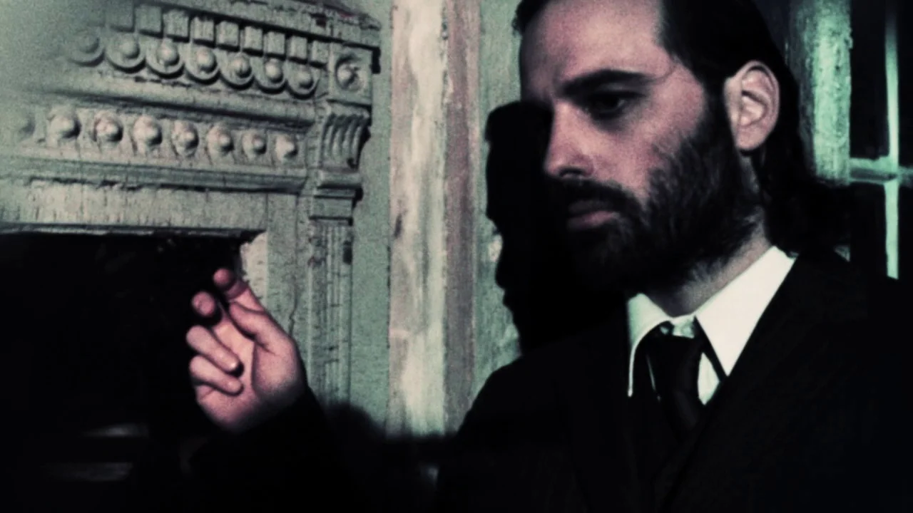 The Forbidden Room (2015) movie still: closeup — A dimly lit interior features a man standing before elaborate carved plaster wall molding. He keeps…