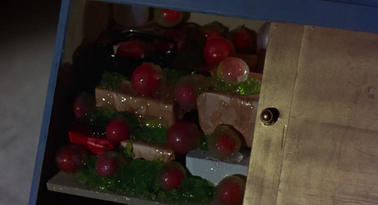 Queen of Blood (1966) movie still: closeup — A refrigerator shelf contains brown rectangular blocks covered in red spheres and green jelly. The door…