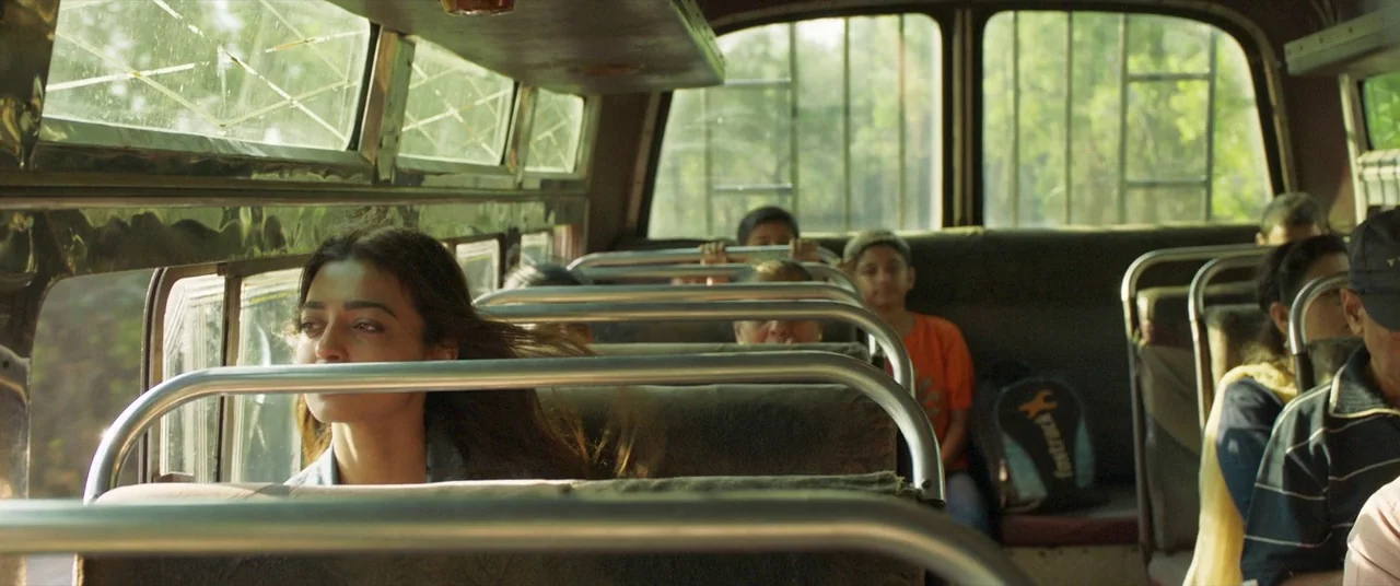 The Wedding Guest (2018) movie still: medium — The interior of a public bus with metal frame seats and large windows. A young woman sits by the…
