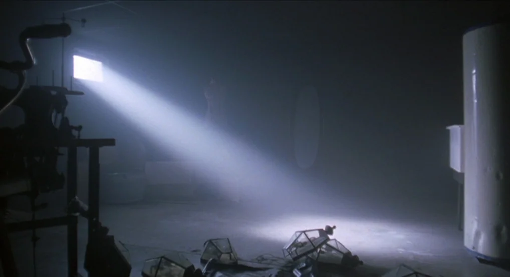 Brick (2005) movie still: wide — A dark, dust-filled attic space with cluttered floor objects and heavy shadow. A single concentrated beam of light…