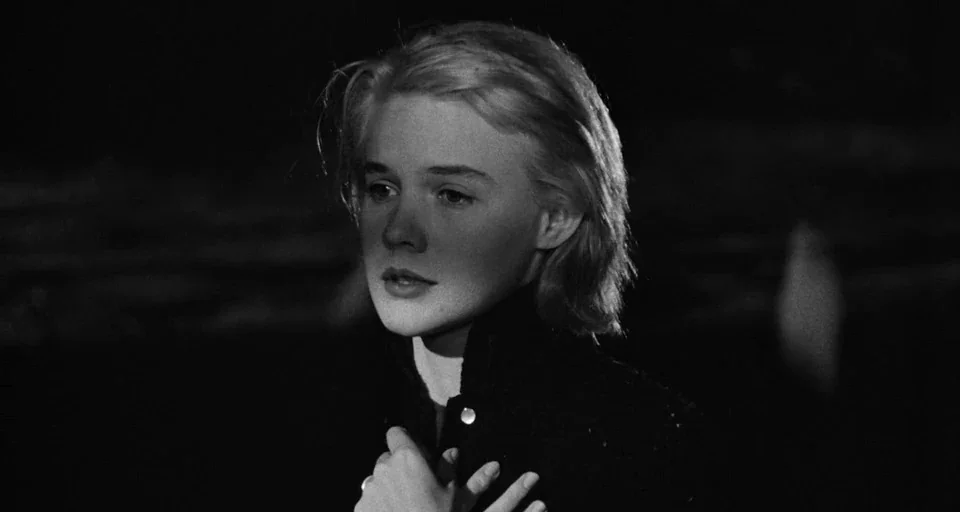 Baby Doll (1956) movie still: closeup — A dark, dimly lit beach environment at night with a stark black backdrop. A woman with short blonde hair…