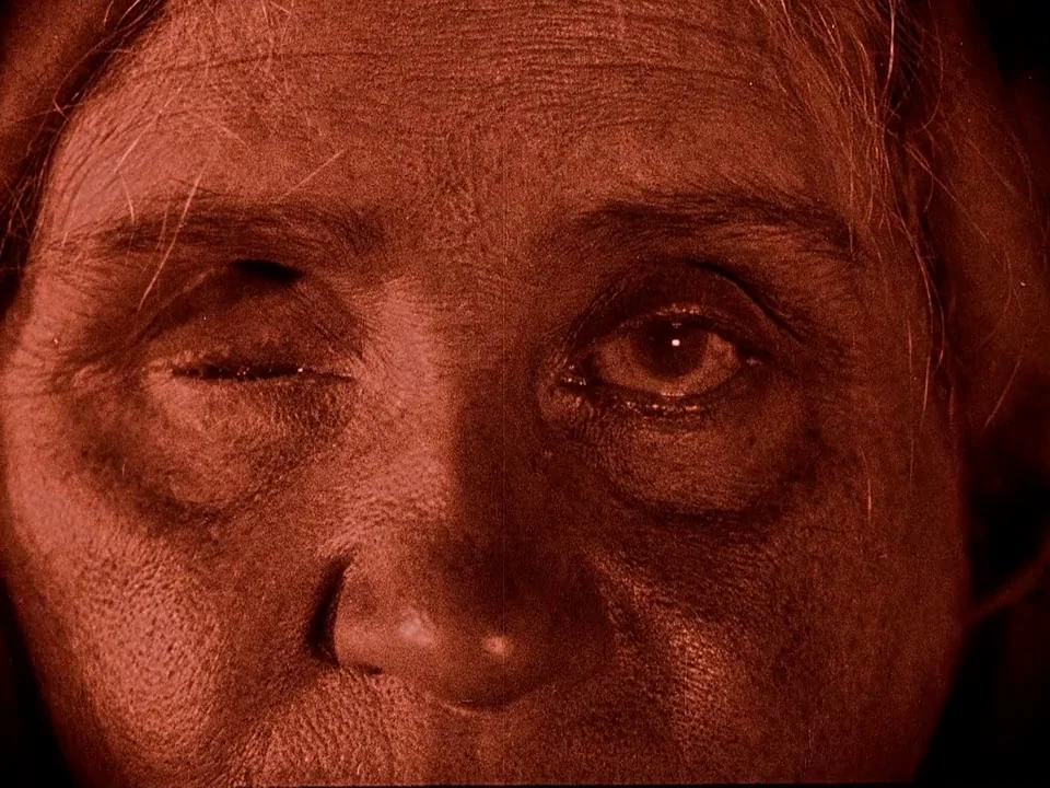 Häxan (1922) movie still: closeup — A close-up view shows the textured face of an elderly woman. She keeps one eye open while the other is closed.