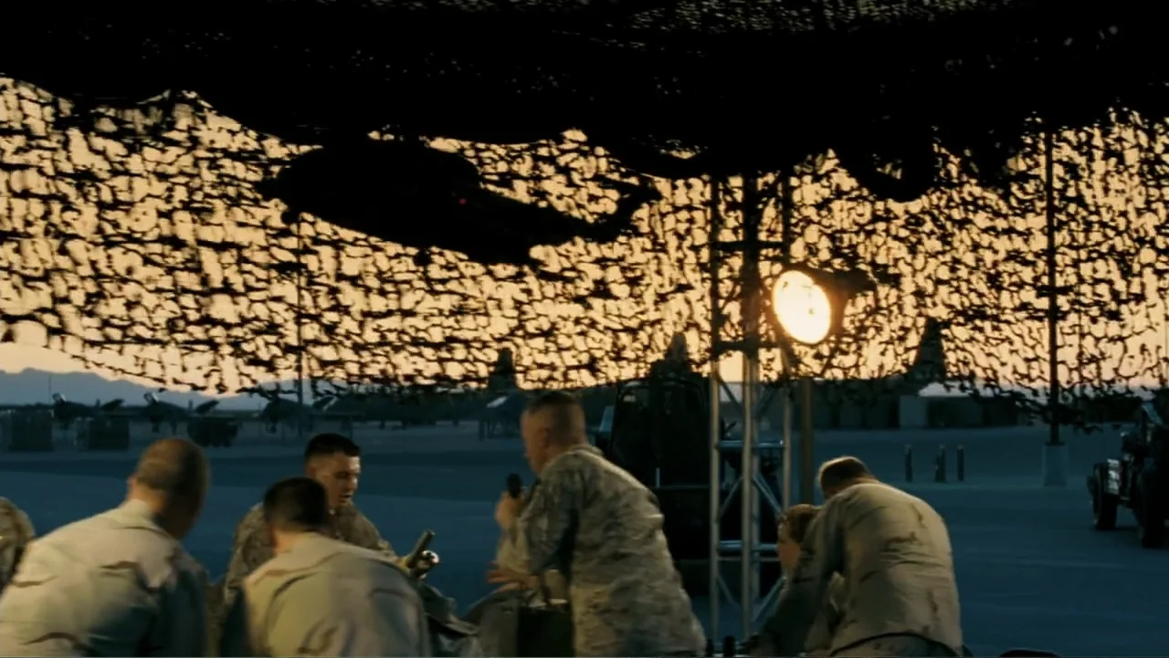 Transformers (2007) movie still: medium — A military airfield at sunset with a group under a large camouflage net. Multiple soldiers in tactical…
