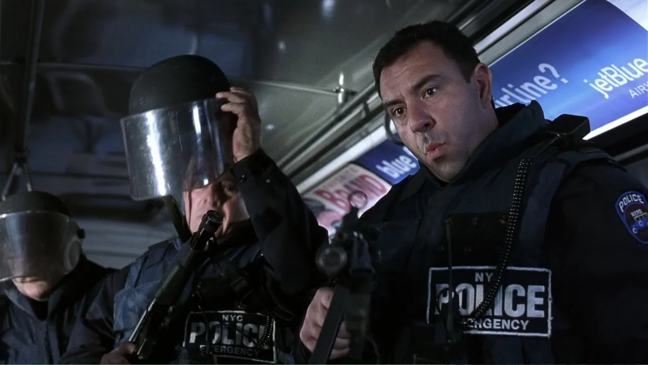 Analyze That (2002) movie still: medium — The interior of a brightly lit subway train car features blue advertisements on walls. Two tactical police…